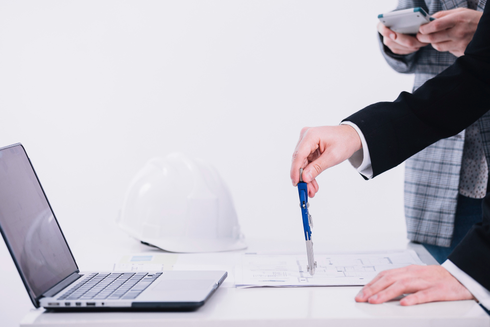 مخططًا معماريًا باستخدام الكمبيوتر وأدوات هندسية مع خوذة حماية على الطاولة - كيان للاستشارات الهندسية.